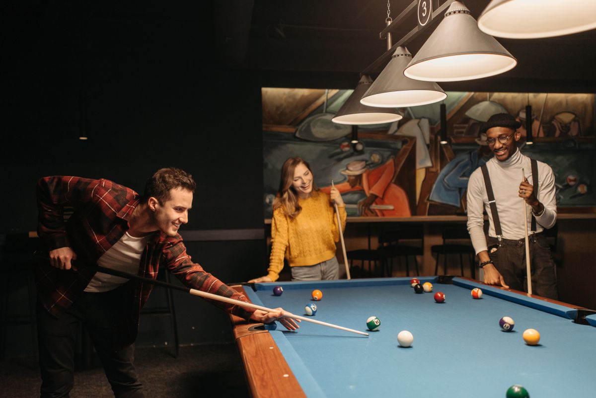 Three friends laughing together around a pool table